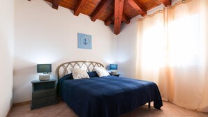 Un dormitorio con cama, dos mesitas de noche, lámpara de pared y techo con vigas a la vista.