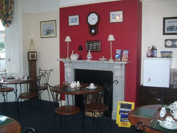 A hotel room with a fireplace, a clock, and a dining area with tables and chairs. - Boaters Guesthouse (Weymouth)
