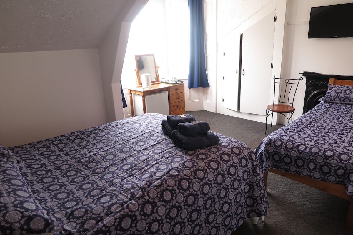 A bedroom with two beds, a desk, a chair, a mirror, and a TV.