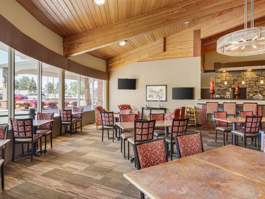 A restaurant with wooden ceiling beams, large windows, and a stone wall backsplash.
