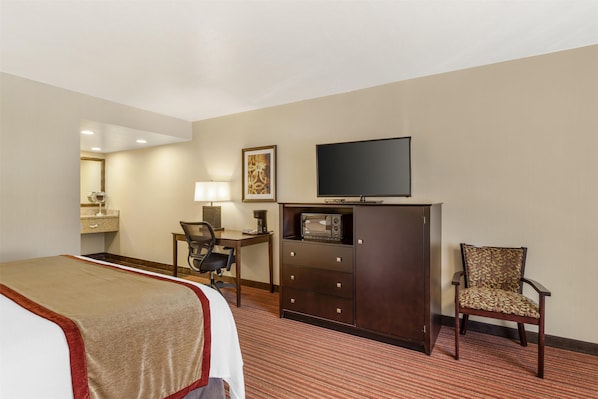 Una habitación de hotel con una cama, un escritorio con silla, un televisor y un armario.
