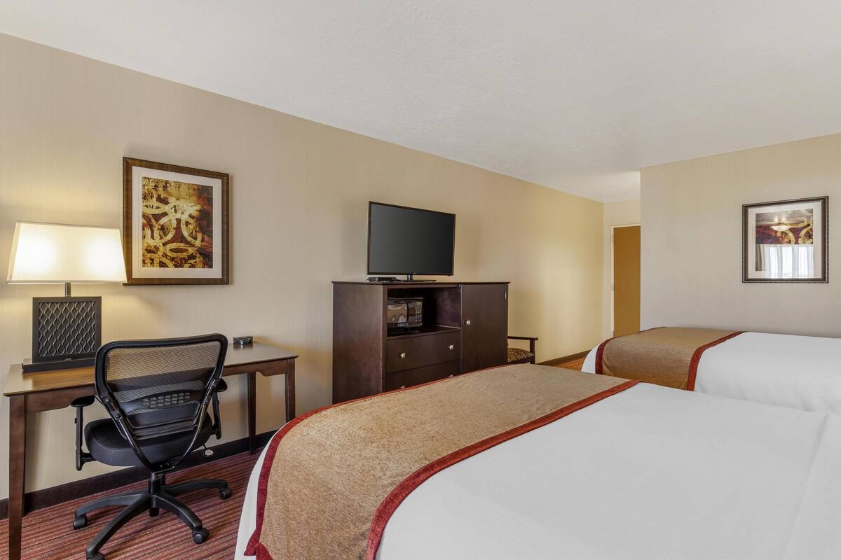 A hotel room with two beds, a desk with a chair, a television, and artwork on the walls.
