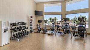 Ein Fitnessstudio mit Trainingsgeräten, einem Fernseher und großen Fenstern.