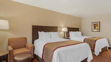 A hotel room with two beds, a chair, a small table, and a lamp.