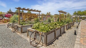 Ein Garten mit erhöhten Beeten, hölzernen Pergolen und einem alten Karren.