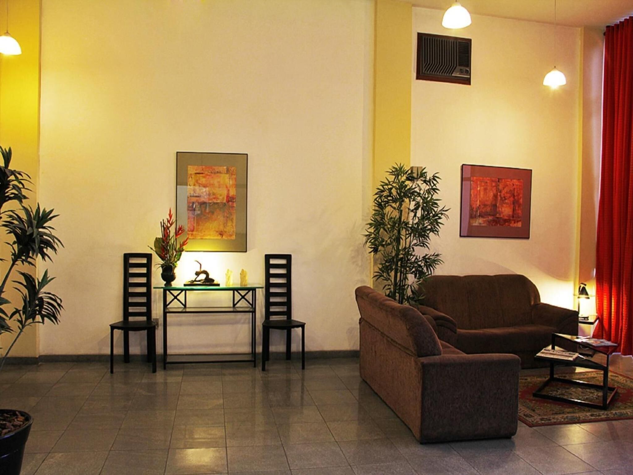 A living room with a brown sofa, a glass coffee table, a small table with two chairs, and two potted plants.