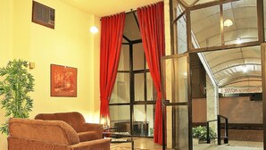 A lobby with a sofa, a potted plant, a framed picture, and a glass door leading to an outdoor area. - Scala Residence Hotel (Resende)