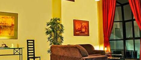 Una habitación con un sillón marrón, una mesita con una lámpara y dos cuadros en la pared.