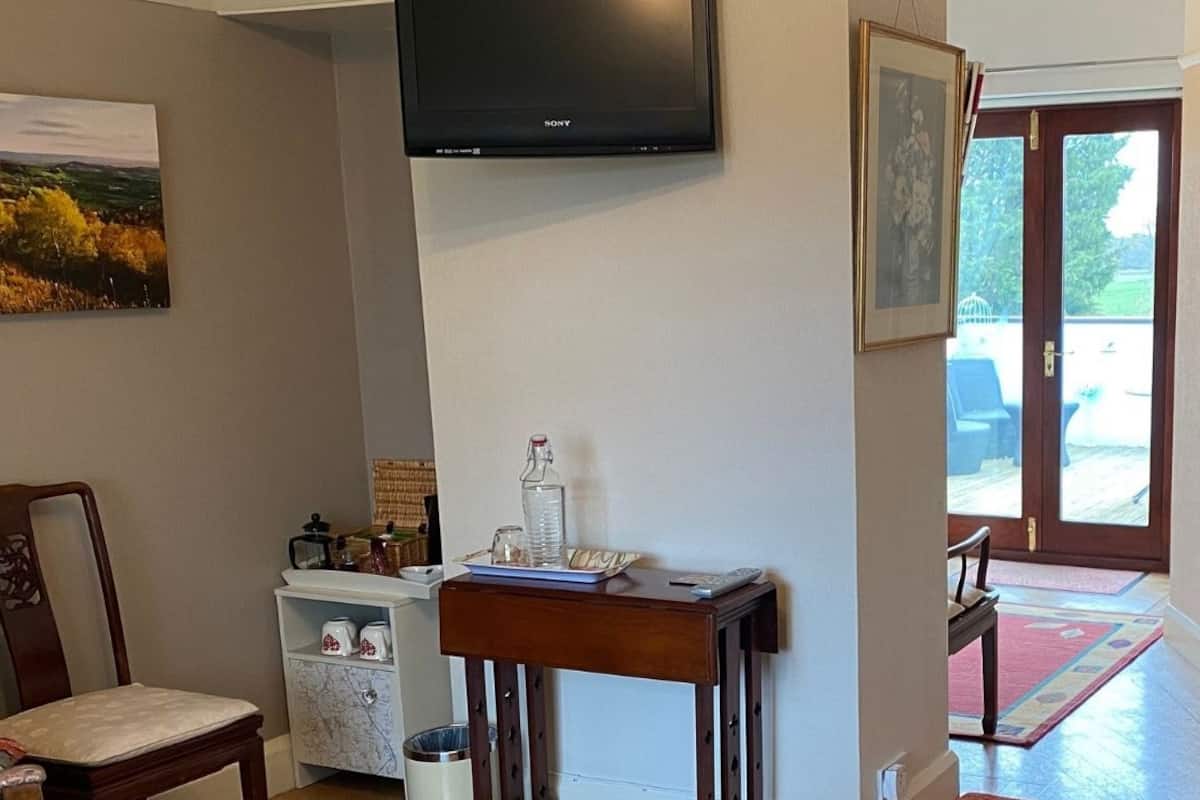 A hallway with a wooden chair, a small table with a glass pitcher, a white cabinet, and a flat-screen TV mounted on the wall.