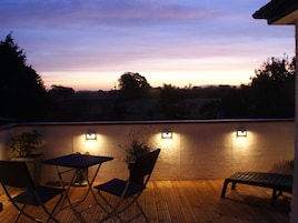 Una terraza de madera con vistas al atardecer, un banco y dos sillas.