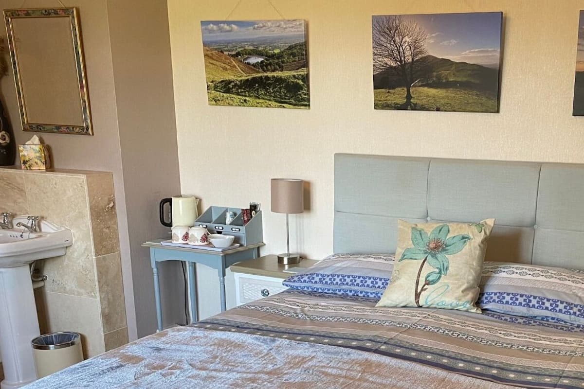 A bedroom with a bed, bedside tables, a nightstand, a mirror, and wall art.