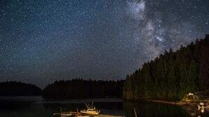 Stjerneskjær over en rolig sø med både fortøjet ved en bro, omgivet af tæt skov.