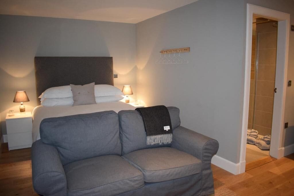 Une chambre à coucher avec un lit, des lampes de chevet, un canapé gris et un porte-manteau en bois.