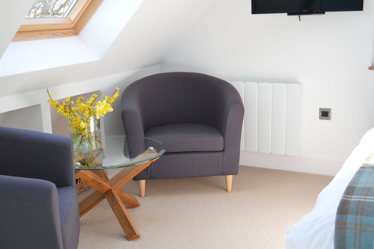A modern room with a grey armchair, a glass coffee table, and a vase with yellow flowers.