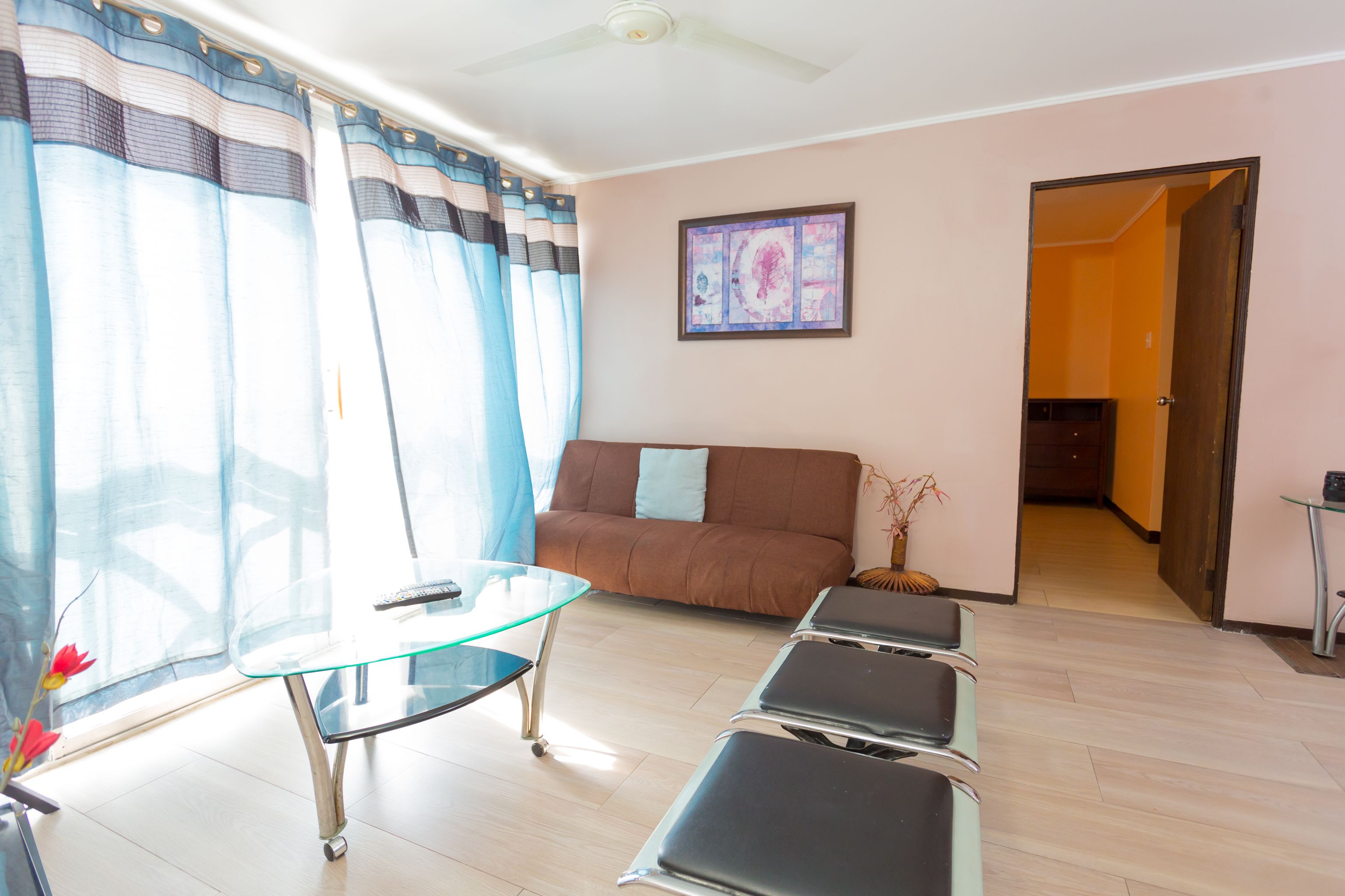 A living room with a glass coffee table, a brown sofa, and a door leading to another room.