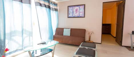 A living room with a glass coffee table, a brown sofa, and a door leading to another room.