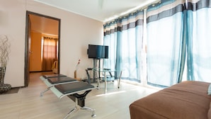 Een hotelkamer met een bed, een bureau met stoel, een televisie en een groot raam met gordijnen.
