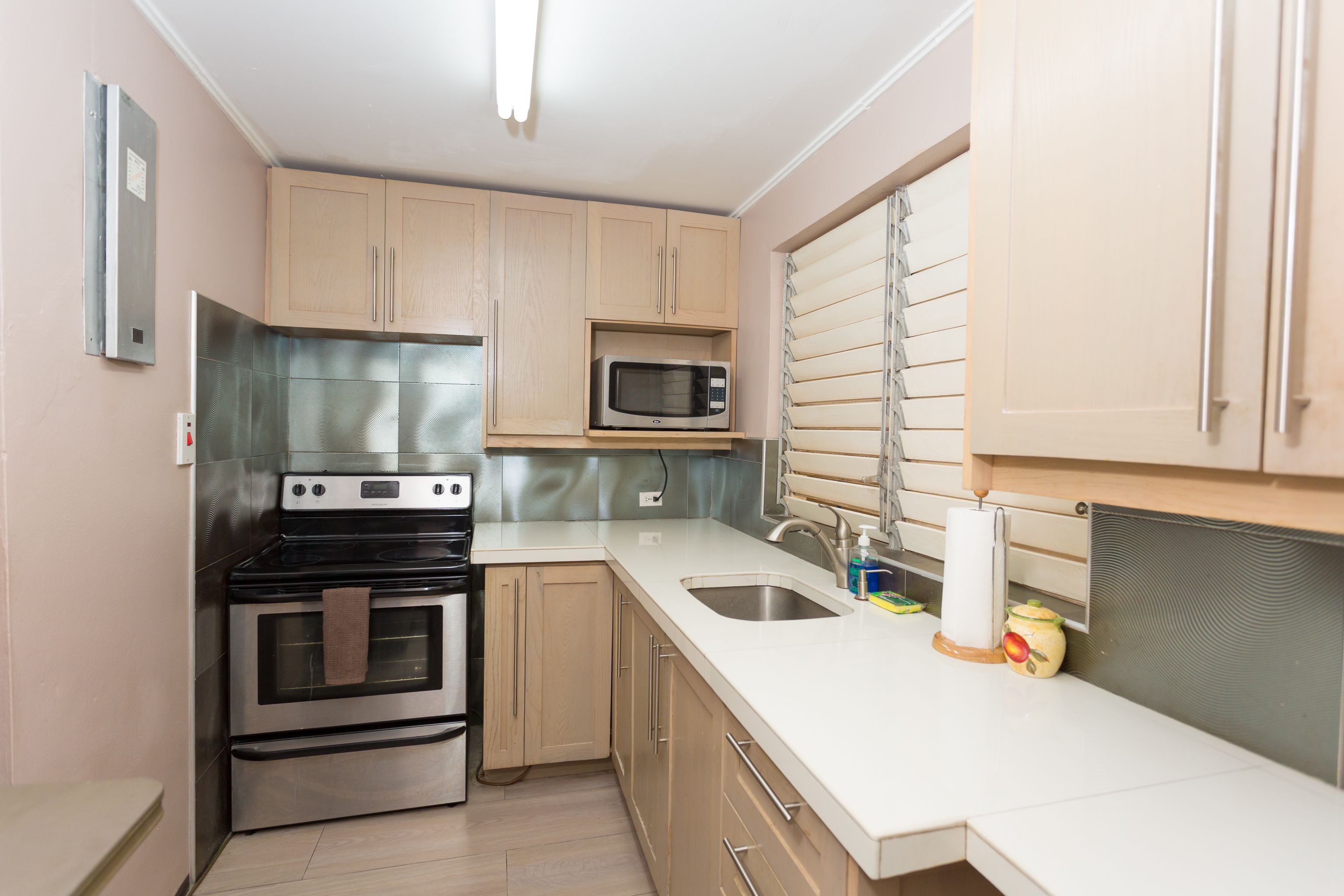 A compact kitchen with stainless steel appliances, wooden cabinets, and a white countertop.