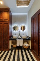 Un baño con dos lavamanos, armarios de madera, piso de baldosas blanco y negro y un tragaluz.
