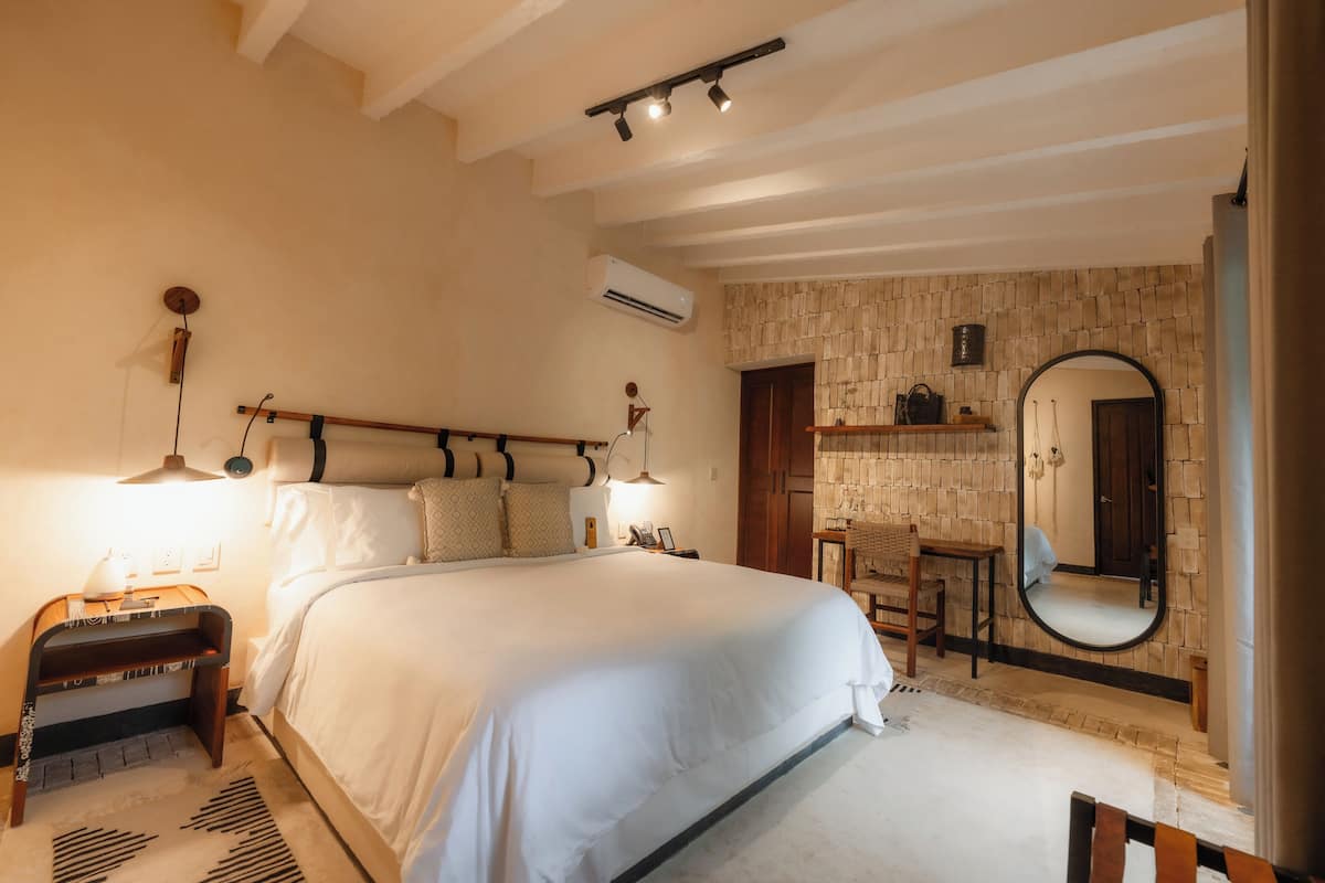 Une chambre à coucher avec un grand lit, une table de chevet avec une lampe, un miroir et une petite chaise en bois.