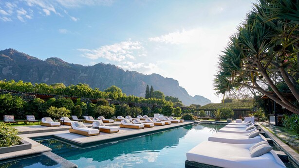 A pool area with lounge chairs and a view of mountains. - Hotel Amomoxtli (Tepoztlán)