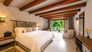 A bedroom with a large bed, wooden beams, a desk, and a view of greenery. - Hotel Amomoxtli (Tepoztlán)