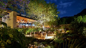 An outdoor dining area with tables and chairs, surrounded by lush greenery and a stone wall. - Hotel Amomoxtli (Tepoztlán)