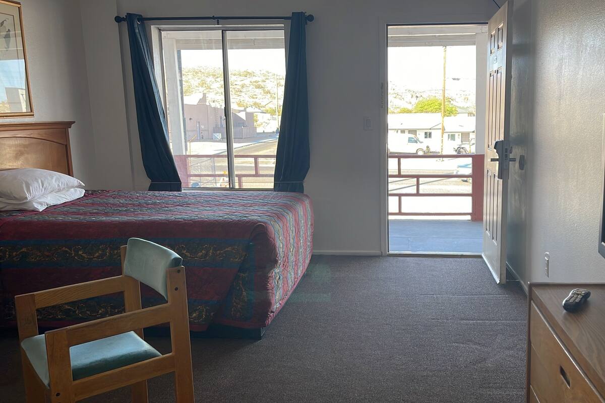 A hotel room with a bed, a chair, a television, and a view of the outside.