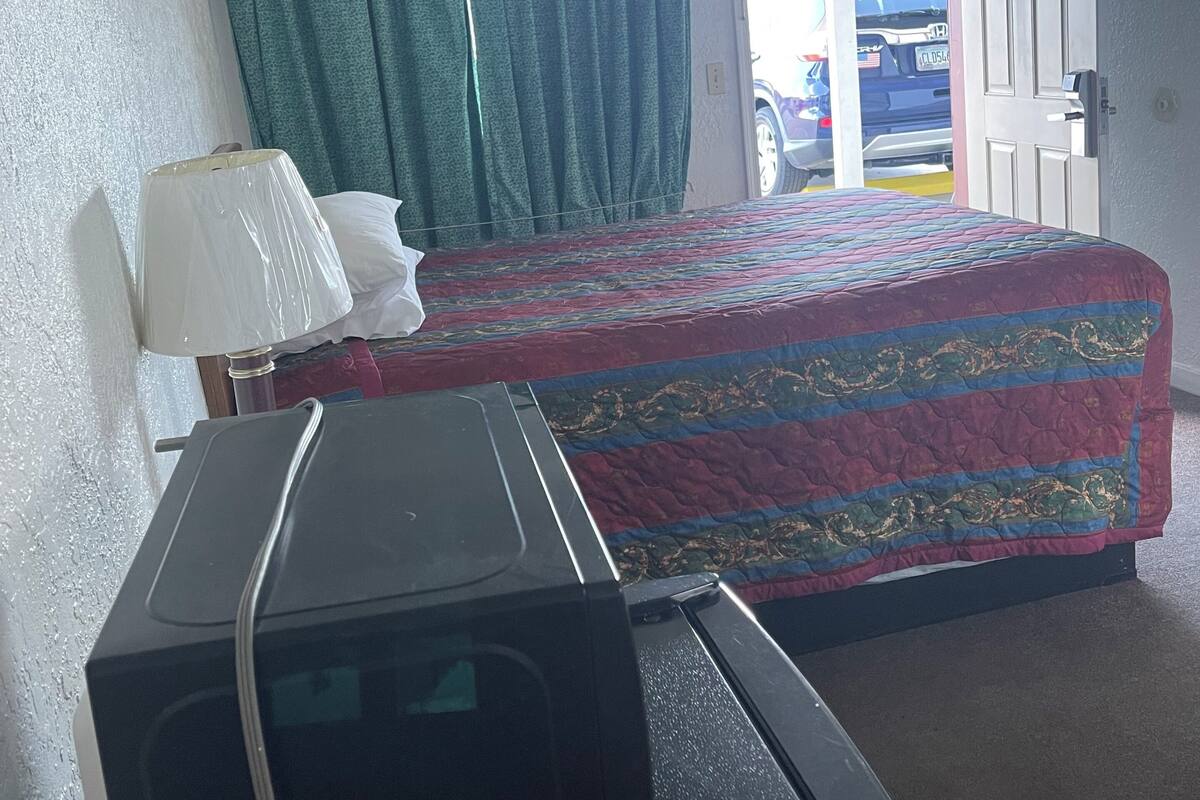 A hotel room with a bed, a television, a window with curtains, and a door leading outside.