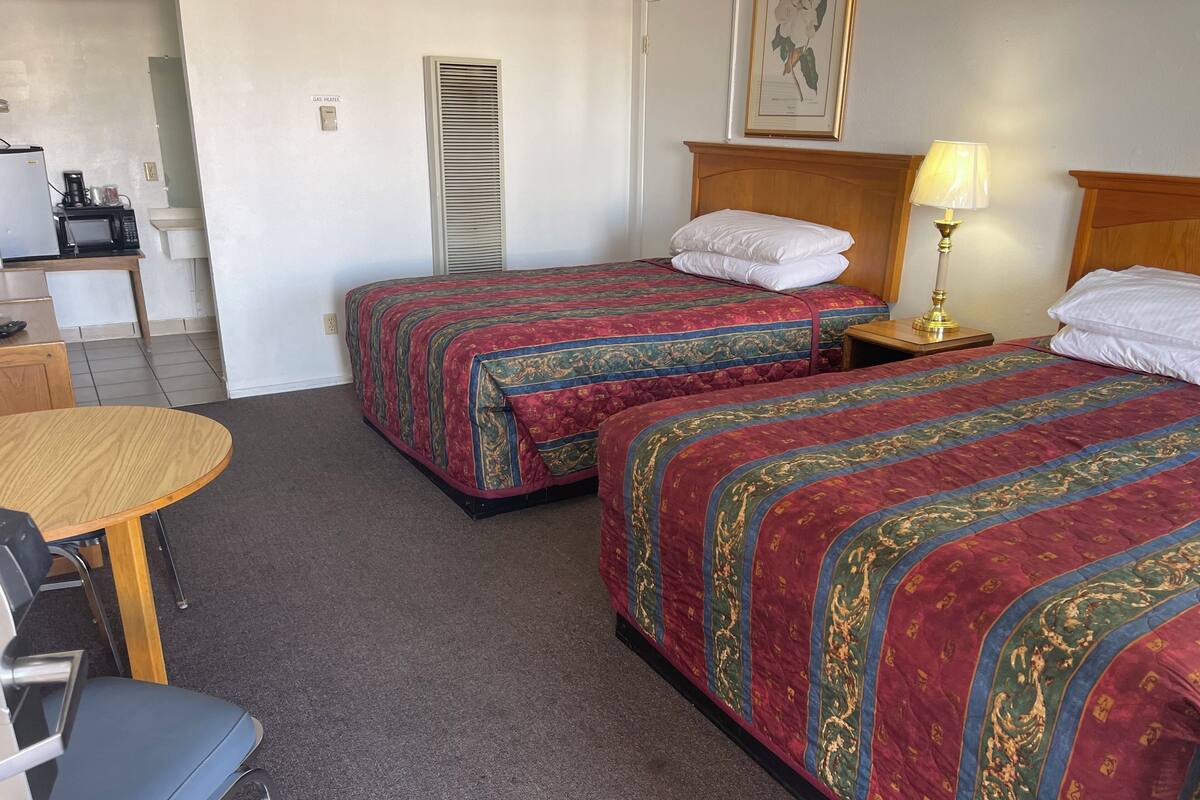 A hotel room with two beds, a desk, a chair, a lamp, and a microwave.