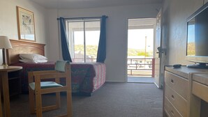 A bedroom with a bed, a chair, a desk, a dresser, a television, and a window with curtains.