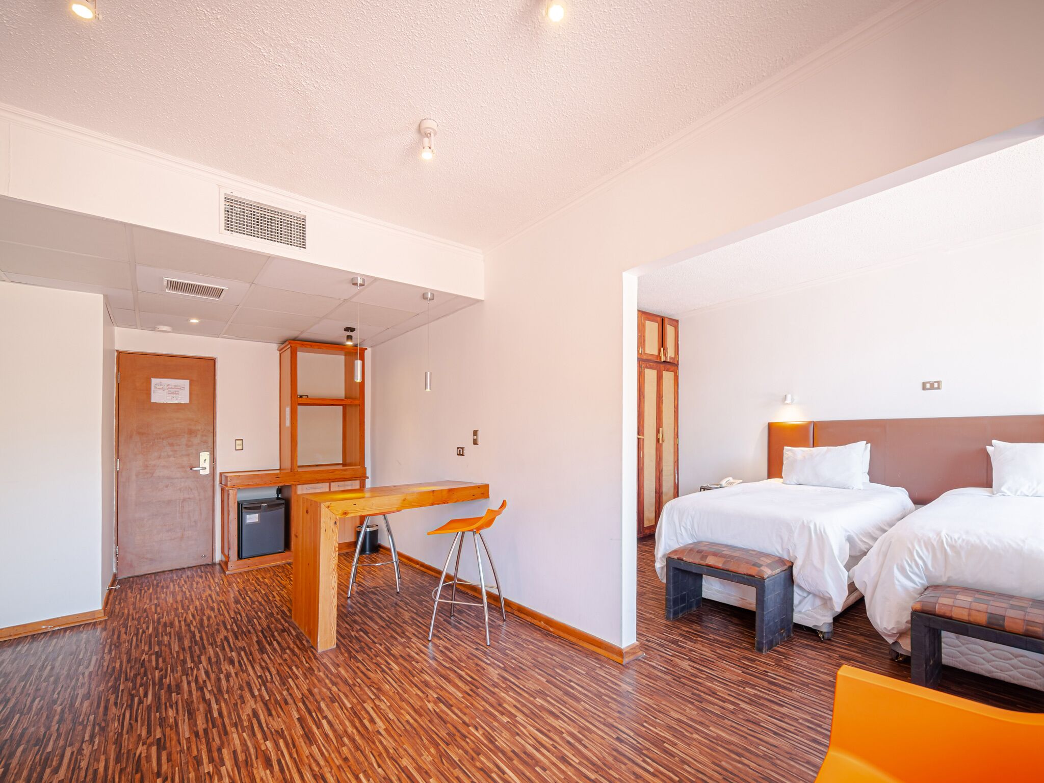 A hotel room with two beds, a wooden desk, and a chair.