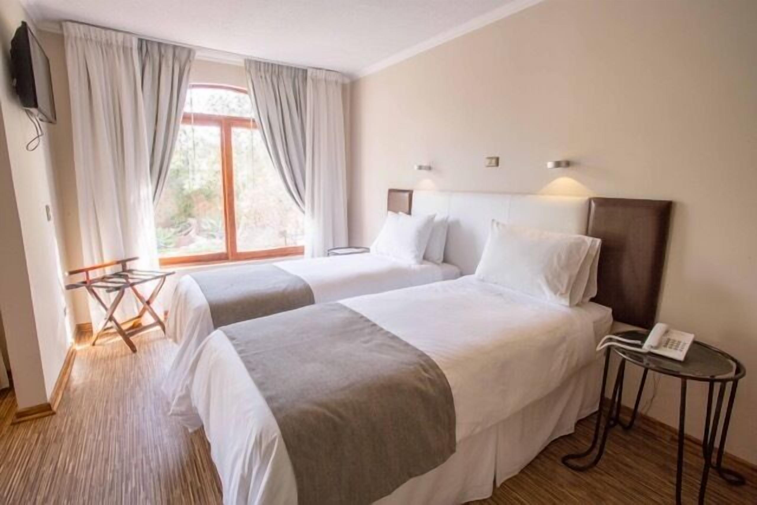 Habitación de hotel con dos camas, una mesita con un teléfono y una ventana con cortinas.