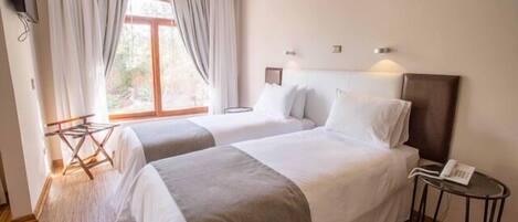 A hotel room with two beds, a small table with a phone, and a window with curtains.