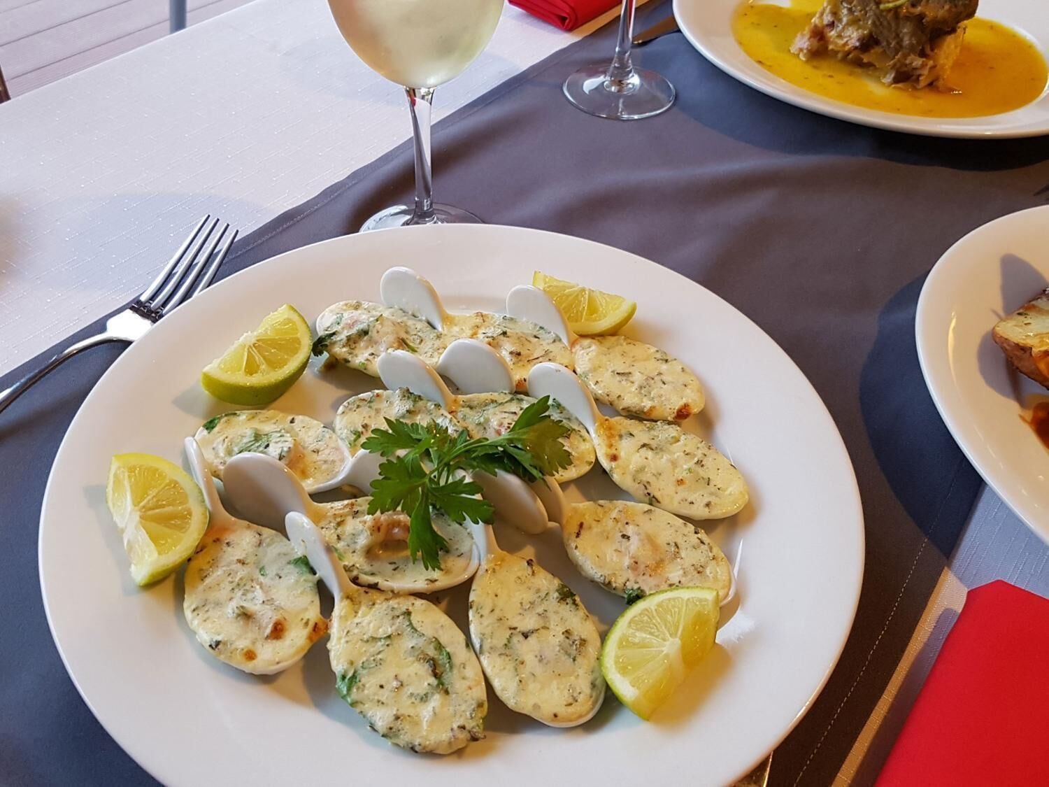 Un plato de comida con rodajas de limón y adorno de perejil, acompañado de una copa de vino blanco.
