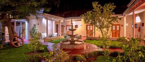 Un patio con una fuente, zona de estar y un edificio con puertas y ventanas.