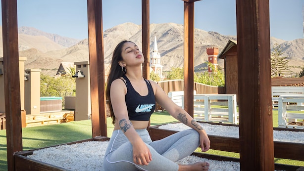 A person sitting on a wooden platform with white pebbles, surrounded by wooden beams and a mountainous landscape in the background. - Terral Hotel & Spa (Vicuña)
