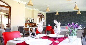 Un comedor con mesas dispuestas para dos, con platos blancos, copas de cristal transparentes y servilletas rojas.