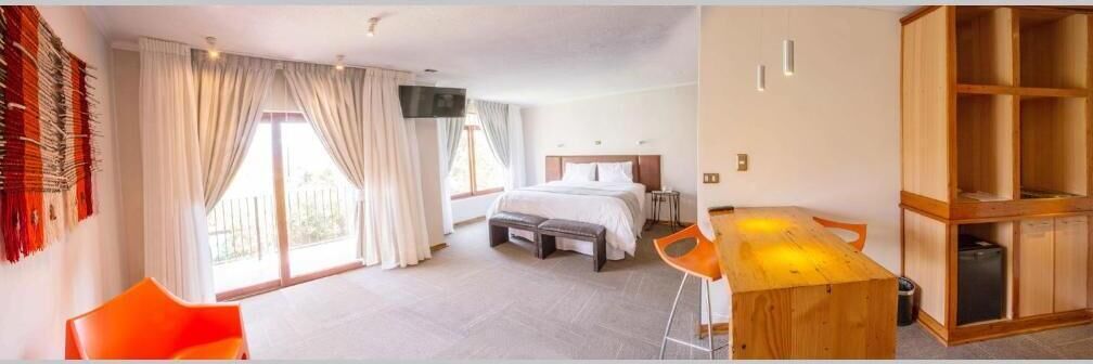 A hotel room with a bed, a desk, and a chair. There is a window with curtains, a television, and a wooden cabinet.