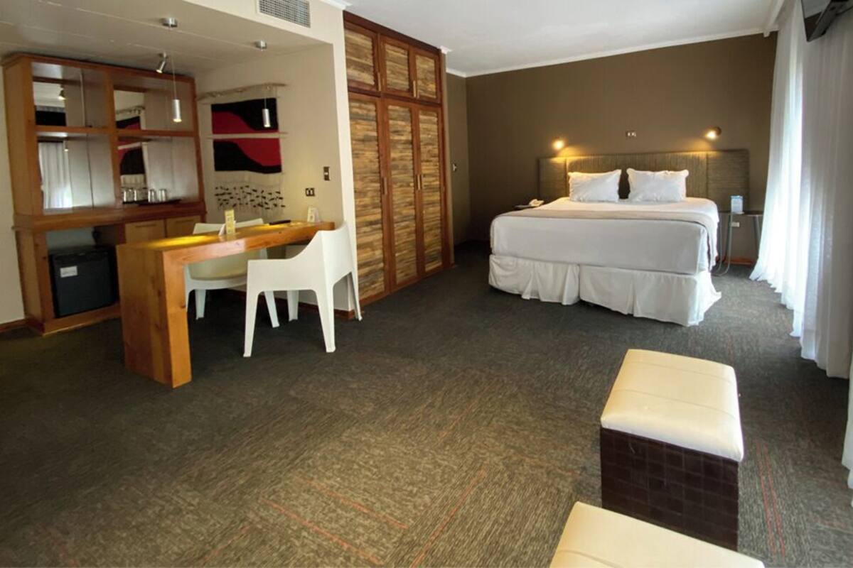 Habitación de hotel con cama, escritorio con silla, armario y una pequeña zona de estar.