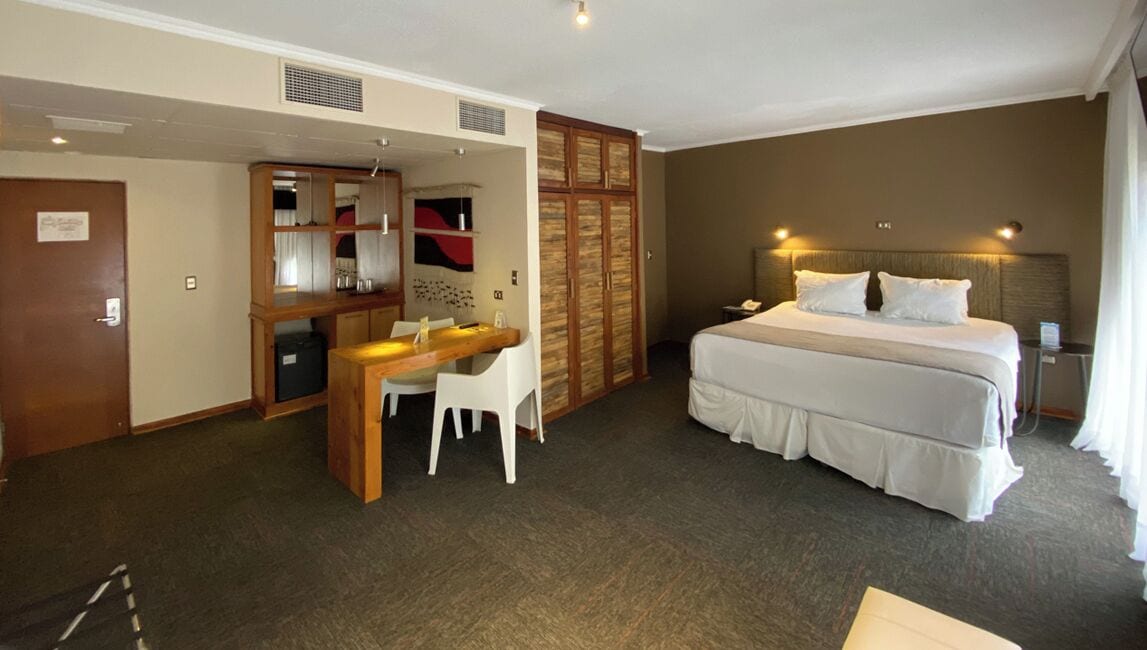Une chambre d’hôtel comprenant un lit, un bureau avec une chaise, une armoire et une petite table.