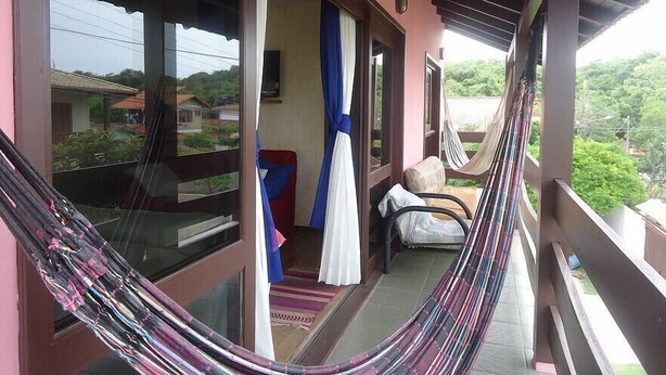 A balcony with a hammock, a chair, and a view of the surrounding area. - Santinho Hostel (Florianópolis)