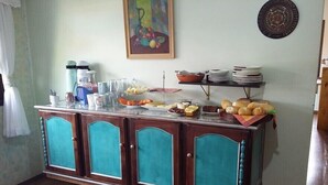A buffet setup with a variety of food items and beverages on a wooden cabinet with teal accents. - Santinho Hostel (Florianópolis)