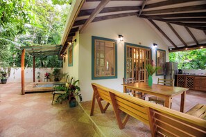 An outdoor patio with a wooden table and benches, surrounded by potted plants and a pergola. - Casa Merlin Lodge (Cahuita)