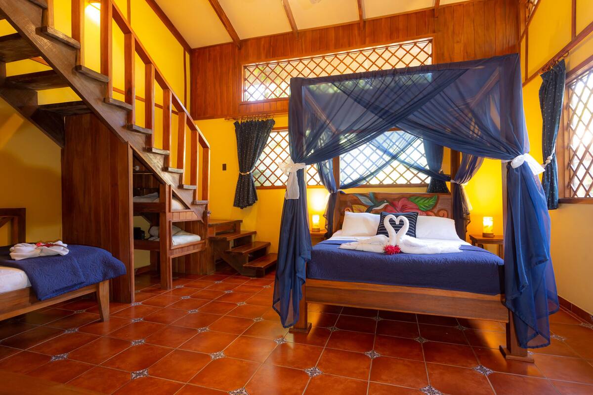 A room with a wooden staircase, a bed with a canopy, and a small seating area.