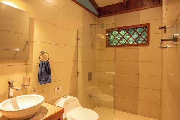 A bathroom with a glass-enclosed shower, a white sink, and a toilet. - Casa Merlin Lodge (Cahuita)