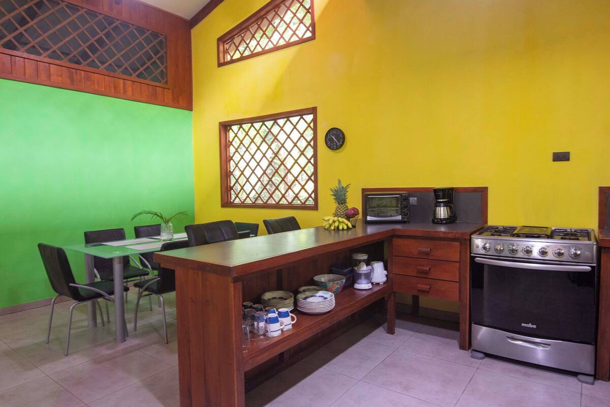 A kitchen with a dining table, chairs, a stove, and a clock on the wall.