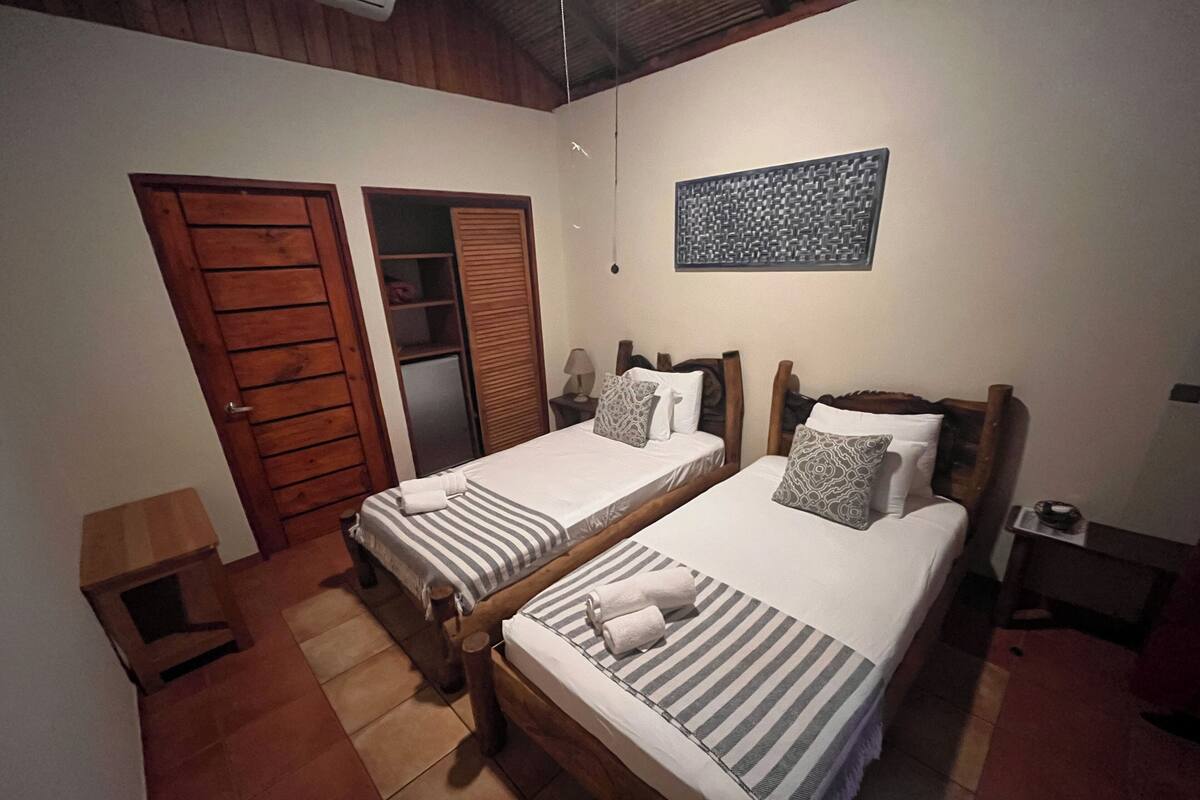 A room with two wooden beds, a wardrobe, a small table, and a wall-mounted artwork.