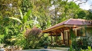 Una piscina con cubierta de madera y una zona de estar techada, rodeada de exuberante vegetación y árboles.