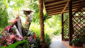 Un espacio al aire libre cubierto con un sendero de piedra, exuberantes plantas tropicales y una estructura de madera celosíaca.